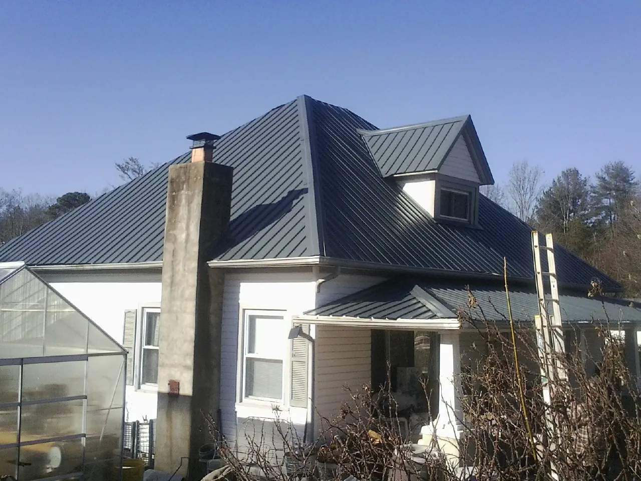 Dark blue standing seam metal roof on a white farmhouse with dormer — Slate & Tile Roof Repair by Roofing Brothers in Mona