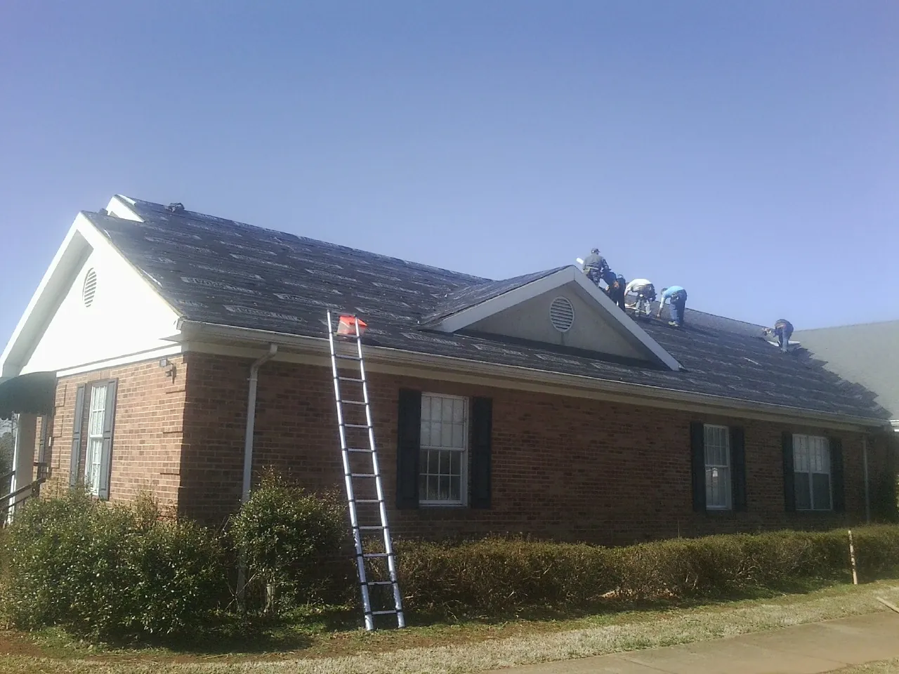 Crew tearing shingles off a brick ranch roof with a ladder set — Metal Roof Repair work by our crew in Mona