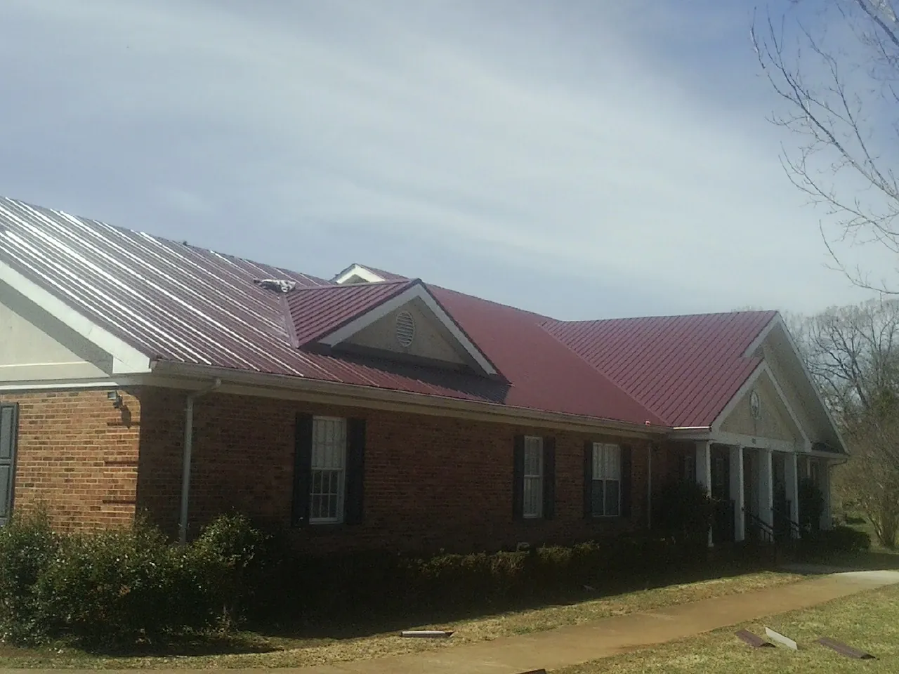 Red metal roof with gabled entries on a long brick building, from a Hail Damage Roof Repair job in Mona