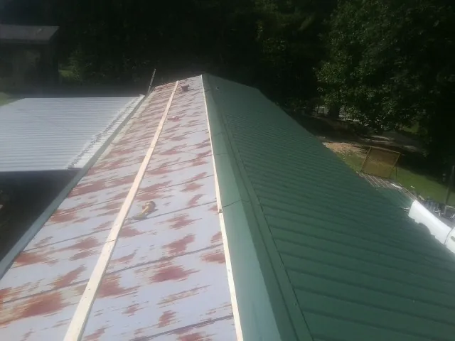 Old rusted panels beside newly installed green metal roofing — Wind Damage Roof Repair by Roofing Brothers in Mona