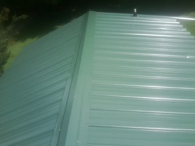 New green metal panels meeting at the ridge of a roof — Flat Roof Repair work by our crew in Mona