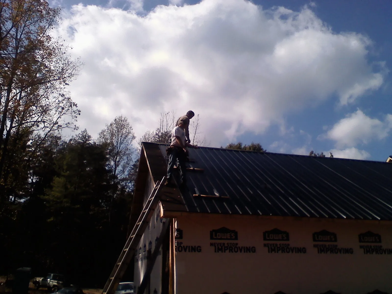 Roofer fastening dark metal panels high against a cloudy sky, from a Roof Inspection job in Mona