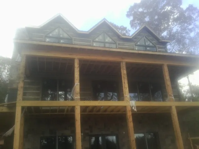 Dormers and porch framing on a large log home under construction — Roof Coating work by our crew in Mona