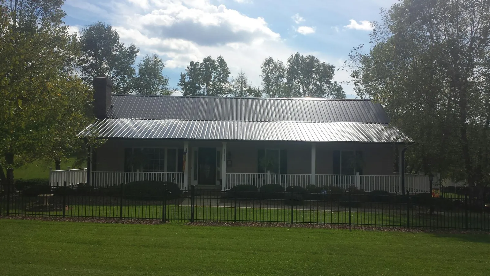 Gray metal roof on a brick ranch with a full width front porch — Gutter Guard Installation work by our crew in Mona