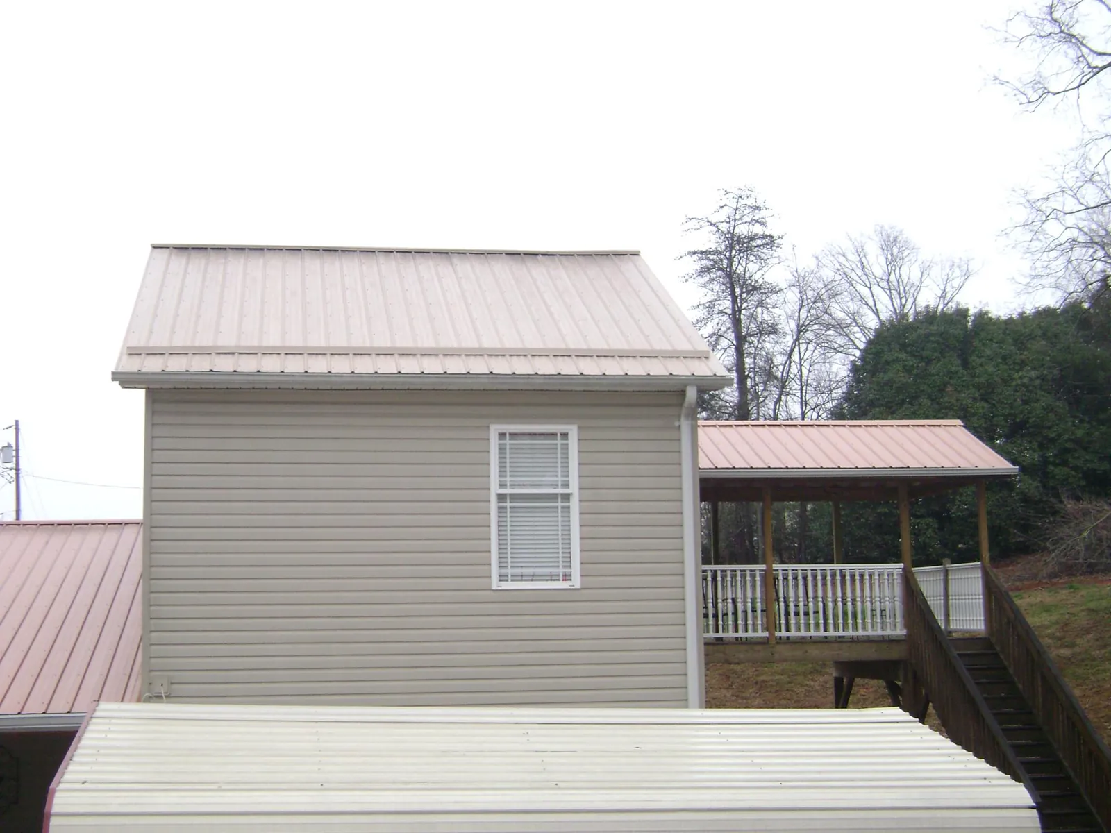 Tan metal roofs on a two story addition and attached porch, from a Roof Replacement job in Mona